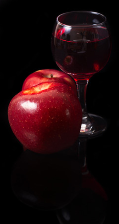 Apples and glass of wine on a black background. Red apples and red wine in a glass glass on the black reflecting background. Vertical shotの写真素材