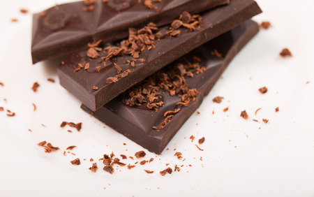 Pieces from a chocolate bar and chocolate crumbs on a white background. Close up, small depth of...