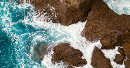 Foamy surf at rocks. The top view, sea waves foam at big coastal stonesの写真素材