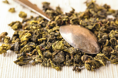 Dry leaves of green tea and teaspoon. A light background from fabric, a close up, selective focus. Grade milk oolong teaの写真素材