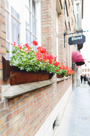 Building fragment of hotel in Bruges. The ancient European city, the brick building, at windows boxes with red colors. In the distance vaguely a street fragment with passersby and cars. Selective focus, the most part of a shot it is bluredの写真素材