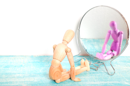 Wooden person Gestalta in front of the mirror. The dummy sits in front of the mirror, in reflection sees itself, but pink color. The person dreamsの写真素材