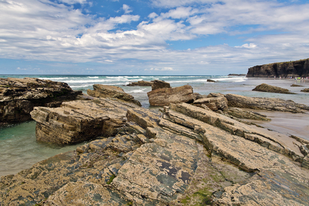 Strip of big stones on the sandy beach during an outflow. Black and gray stones, yellow sand and water of the ocean in the distance. Sunny summer dayの写真素材