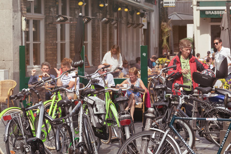 BRUGES, BELGIUM - JUNE 8, 2017: Set of the bicycles parked at street cafe. People behind little tables have a rest, in the foreground in focus bicycles. Sunny summer day, brisk streetのeditorial素材