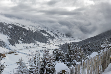 The top view on the road in the mountain valley in Andorra. Winter day, cloudy, clouds crawl over...