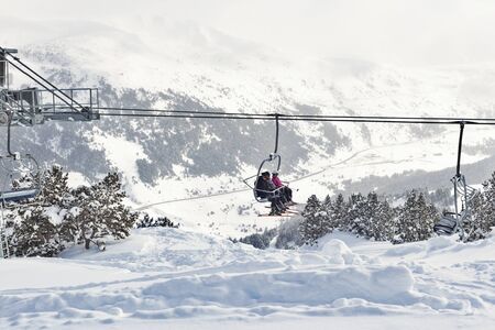 PYRENEES, ANDORRA - FEBRUARY 7, 2018: Skiers on a chairlift in the mountains over deep snow. Snowdrift and Christmas trees in the snow in the foreground, far tops of the mountainsのeditorial素材
