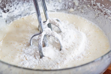 The mixer nozzle is immersed in a pie dough. Close-up, selective focus, floured glass bowlの写真素材