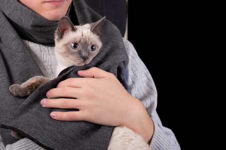 A young man presses a kitten wrapped in a scarf to his chest.の写真素材