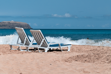 Two empty deck chairs on a deserted sandy beach on the ocean.の写真素材