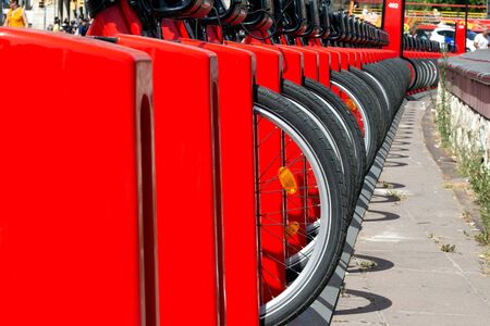 Fragment of a rack with bicycles that can be rented on the street of a European city. Red metal rack, bicycle wheels, close-up, selective focusの写真素材