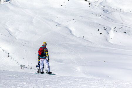 PYRENEES, ANDORRA - FEBRUARY 13, 2019: A snowboarder in bright clothes staands on a mountainside and prepares for the descent.のeditorial素材