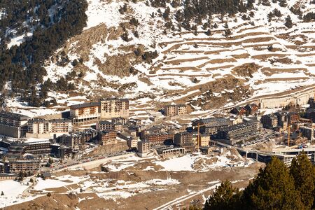 Top view of the modern village in the mountains of Andorra from far away in winter. High-rise buildings, winding road up and mountainsides in the snow with thawedの写真素材