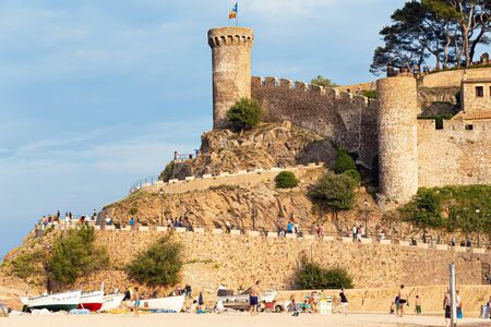 TOSSA DE MAR,SPAIN - AUGUST 7, 2019: An ancient fortress on the beach, tourists on a sandy beach at the foot.のeditorial素材