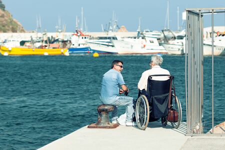 LLORET DE MAR,SPAIN - AUGUST 8, 2019: Two men sit on the edge of the pier on a summer day.