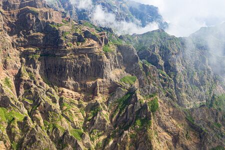 Landscape with a tourist trail in the mountains of Madeira, Portugal on a sunny summer day. High cliffs with clouds in between, fantastic scenery behind every turn, bright vegetationの写真素材