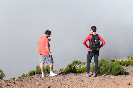MADEIRA, PORTUGAL - JULY 27, 2018: Two tourists, a man and a woman, stand on the edge of a precipice filled with clouds.のeditorial素材