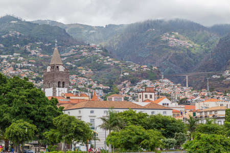 FUNCHAL, MADEIRA - JULY 22, 2018: View of the city centre and houses on the slopes of the mountains on a cloudy summer day. Traditional Portuguese homes and clouds on the topsのeditorial素材