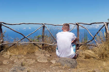 MADEIRA, PORTUGAL - JULY 27, 2018: tourist looks pensively into the distance at the view point. A wooden fence on the edge of a cliff and a clear blue sky on a summer dayのeditorial素材