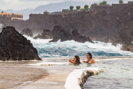 PORTO MONIZ MADEIRA - AUGUST 2, 2018: girls bathes in a natural lava pool during high tides and large waves in the ocean. Lava pools are the main attraction of Porto Moniz. Lava flows, frozen, formed natural backwaters.のeditorial素材