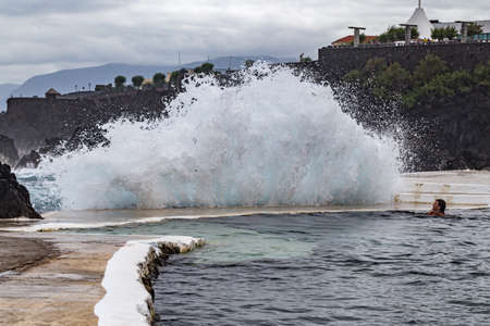 PORTO MONIZ MADEIRA - AUGUST 2, 2018: A girl bathes in a natural lava pool during high tides and large waves in the ocean. Lava pools are the main attraction of Porto Moniz. Lava flows, frozen, formed natural backwaters.のeditorial素材