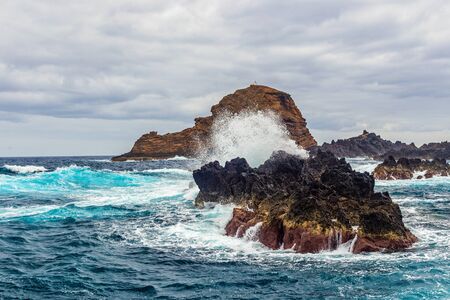 Ocean waves break against coastal cliffs on a cloudy summer dayの写真素材