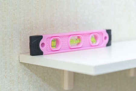 Pink construction level on the shelf in the apartment. A tool in a feminine style, stereotypical...