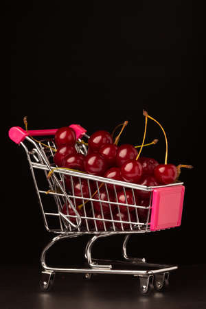 A supermarket cart is filled with ripe red cherries on a black background. Close-up, selective focusの写真素材