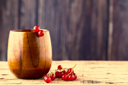 A brush of red currants lies on the table next to a wooden cup.の写真素材