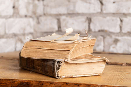 Two old books in a battered binding are lying against a brick wall made of light brick.の写真素材