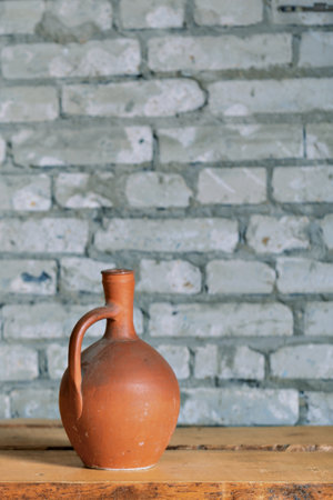 A clay ceramic jug with a high narrow neck against a gray brick wallの写真素材