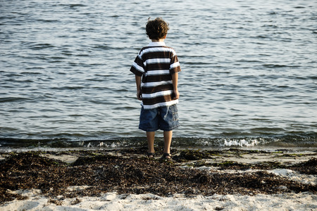 Photo of a Young Boy Standing By The Water - Beach at Duskの写真素材