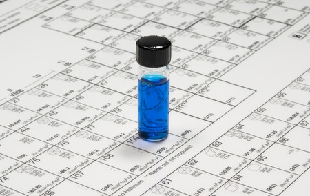 Photo of a Glass Chemical Bottle With Blue Liquid on a Periodic Tableの写真素材