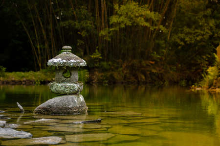 Japanese garden with a stone lantern on a rock in front of a pondの写真素材