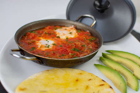 Shakshuka in a frying pan with avocado and pita breadの写真素材