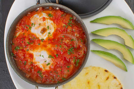 Baked fish with tomato sauce and avocado in pan on black backgroundの写真素材