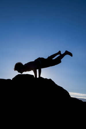 Young man making equilibria exercise on the top of the rock with natural back light  の写真素材