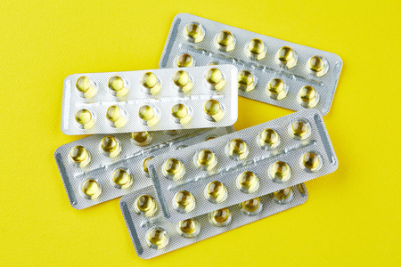 Sealed packages with transparent capsules on yellow background. Vitamins.