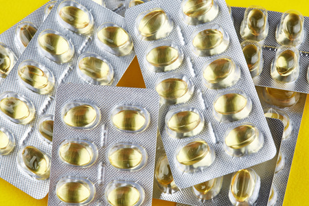Sealed packages with transparent capsules on yellow background. Vitamins.の写真素材