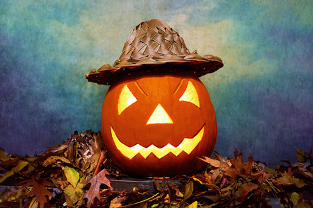 Glowing Halloween pumpkin in wicker hat on heap of leaves.の写真素材
