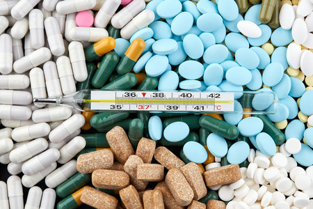 Thermometer on blue pills and colorful capsules. Medicine.