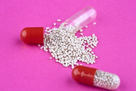 Close-up photo of open capsule with medicine on pink background.