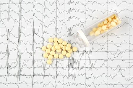 Close-up photo of yellow pills and vial on EKG graph.
