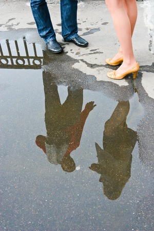 Man and woman are talking and are reflected in a puddle near their feet
