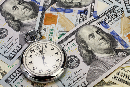 Stopwatch lays on hundred dollar bills.
