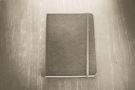 Vintage sepia color : Old hardcover notebook with strip on wood table.の写真素材