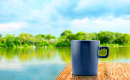 blue Coffee cup on wood table at blur tree and lagoon background.の写真素材