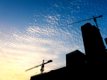 Silhouette of sunset scene with tower crane on the construction site building in city.の写真素材