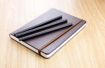Three Black pencil on Brown Hard cover notebook with elastic strap on wooden table in perspective view.の写真素材