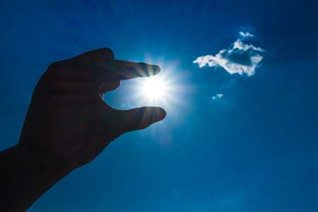 Silhouette of Hand picking sun at blue sky and cloud.の写真素材