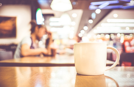 Vintage filter, White coffee cup on wood table with blurred cafe bokeh light background.の写真素材